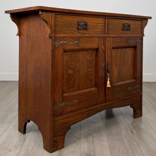 fig 8. An Arts and Crafts golden oak sideboard featuring two top drawers, two lower cupboard doors, and stylized copper strap hinges.