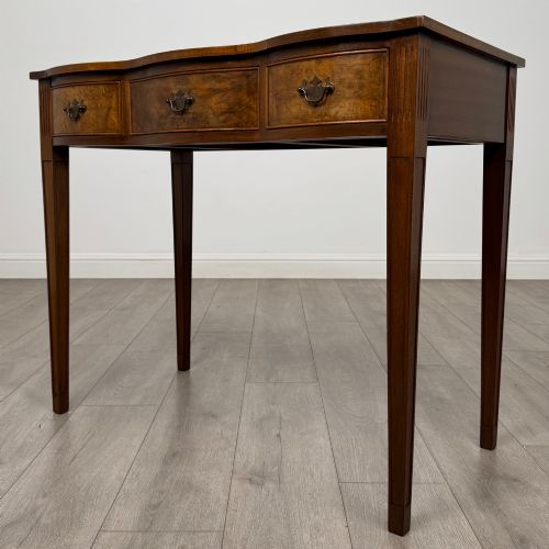 fig 1. A 20th-century burr walnut side table featuring a serpentine front, three drawer fronts with brass handles, and square tapered legs.