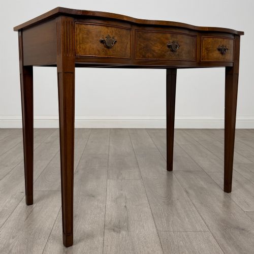 fig 7. A 20th-century burr walnut side table featuring a serpentine front, three drawer fronts with brass handles, and square tapered legs.
