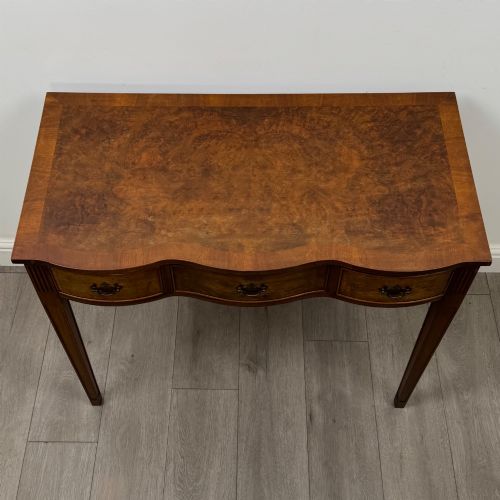 fig 8. A 20th-century burr walnut side table featuring a serpentine front, three drawer fronts with brass handles, and square tapered legs.