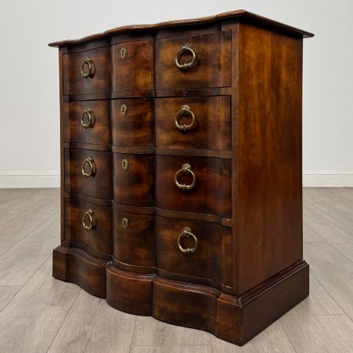fig 1. A 20th-century serpentine-front hardwood chest featuring four stacked drawers with brass drop ring handles and central brass escutcheons.