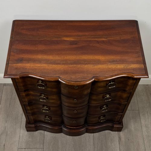 fig 8. A 20th-century serpentine-front hardwood chest featuring four stacked drawers with brass drop ring handles and central brass escutcheons.