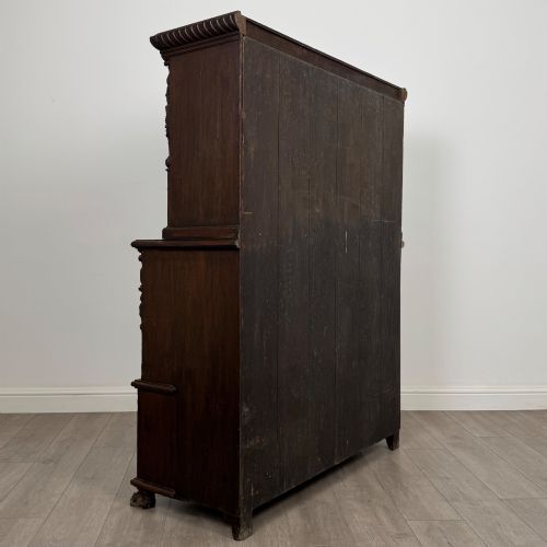 fig 4. A 19th-century dark oak carved cupboard featuring an open top shelf, carved lion cresting, relief-carved panel doors with figures, and an open lower base.