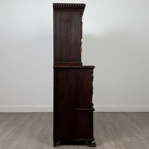 fig 7. A 19th-century dark oak carved cupboard featuring an open top shelf, carved lion cresting, relief-carved panel doors with figures, and an open lower base.