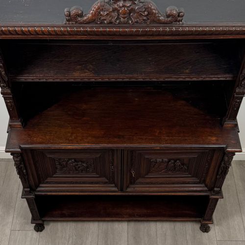 fig 9. A 19th-century dark oak carved cupboard featuring an open top shelf, carved lion cresting, relief-carved panel doors with figures, and an open lower base.