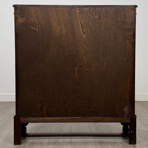 fig 5. An Edwardian dark oak display cabinet with double diamond-leaded glass doors, a carved scroll frieze along the top, interior wooden shelves, and bulbous turned legs connected by a stretcher.