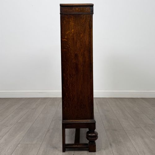 fig 7. An Edwardian dark oak display cabinet with double diamond-leaded glass doors, a carved scroll frieze along the top, interior wooden shelves, and bulbous turned legs connected by a stretcher.