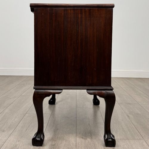 fig 6. A dark mahogany chest of drawers featuring three long drawers with brass handles, raised on carved cabriole legs ending in ball and claw feet.