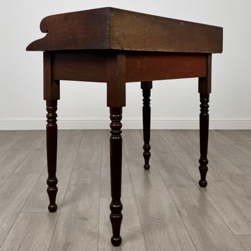 fig 3. A 19th-century dark mahogany writing table featuring a raised gallery back upstand, two frieze drawers with turned handles, and four turned legs.
