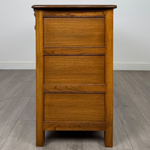 fig 3. A warm brown solid oak sideboard with three drawers positioned above three fielded panel cupboard doors.