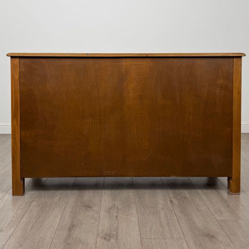 fig 5. A warm brown solid oak sideboard with three drawers positioned above three fielded panel cupboard doors.