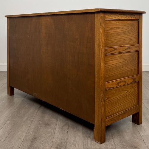 fig 6. A warm brown solid oak sideboard with three drawers positioned above three fielded panel cupboard doors.