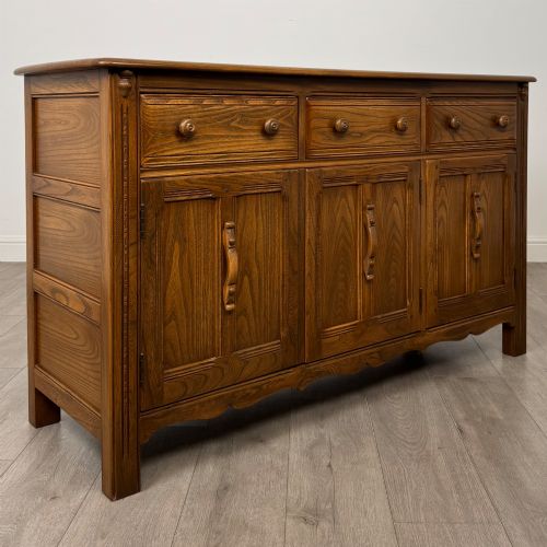 fig 8. A warm brown solid oak sideboard with three drawers positioned above three fielded panel cupboard doors.