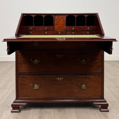 fig 1. An 18th-century Georgian mahogany bureau featuring a sloped fall-front lid, brass batwing handles and escutcheons, three graduated drawers, and bracket feet.