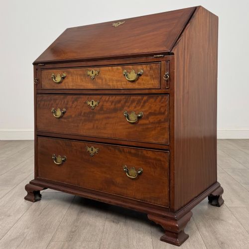 fig 2. An 18th-century Georgian mahogany bureau featuring a sloped fall-front lid, brass batwing handles and escutcheons, three graduated drawers, and bracket feet.