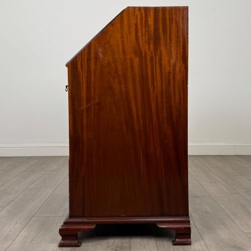 fig 3. An 18th-century Georgian mahogany bureau featuring a sloped fall-front lid, brass batwing handles and escutcheons, three graduated drawers, and bracket feet.