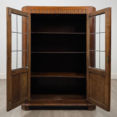 fig 1. A twin-door dark oak display cabinet featuring leaded glass upper panels, carved decorative lower panels, and ornate metal hinges.