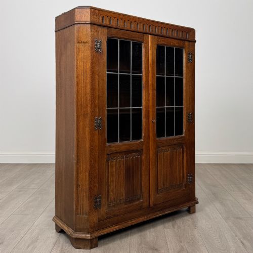 fig 8. A twin-door dark oak display cabinet featuring leaded glass upper panels, carved decorative lower panels, and ornate metal hinges.