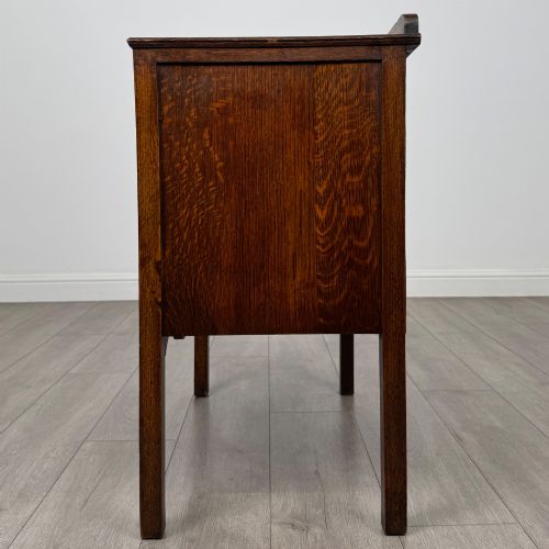 fig 2. An antique golden oak chest of drawers featuring two wide drawers with stylised dark metal handles and a scalloped lower apron.