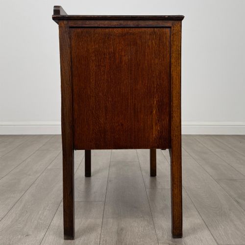 fig 6. An antique golden oak chest of drawers featuring two wide drawers with stylised dark metal handles and a scalloped lower apron.