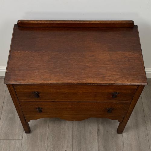 fig 8. An antique golden oak chest of drawers featuring two wide drawers with stylised dark metal handles and a scalloped lower apron.