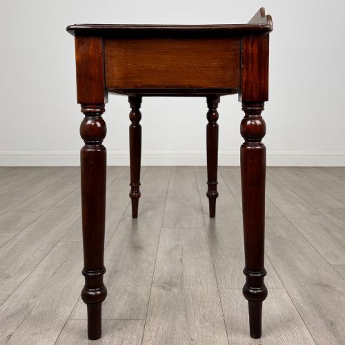 fig 2. A Victorian mahogany writing table featuring two frieze drawers with brass ring handles and four turned legs.