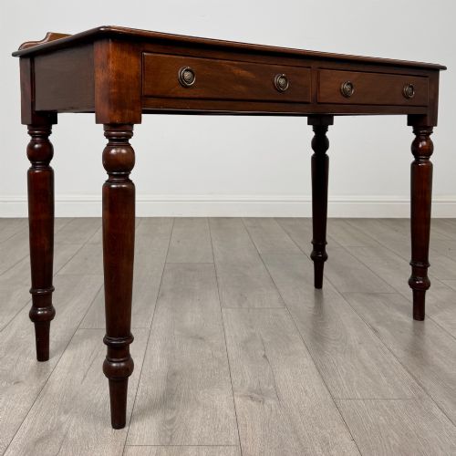 fig 7. A Victorian mahogany writing table featuring two frieze drawers with brass ring handles and four turned legs.