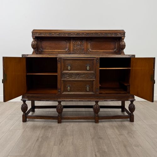 fig 1. A dark carved oak sideboard featuring a raised gallery back, geometric octagonal panel doors, two central drawers with brass handles, and bulbous turned legs.