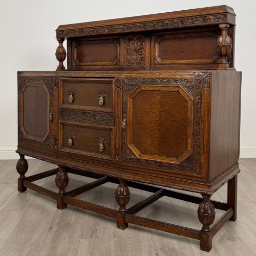 fig 2. A dark carved oak sideboard featuring a raised gallery back, geometric octagonal panel doors, two central drawers with brass handles, and bulbous turned legs.
