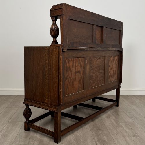 fig 4. A dark carved oak sideboard featuring a raised gallery back, geometric octagonal panel doors, two central drawers with brass handles, and bulbous turned legs.