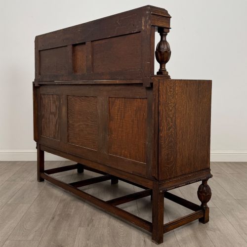 fig 6. A dark carved oak sideboard featuring a raised gallery back, geometric octagonal panel doors, two central drawers with brass handles, and bulbous turned legs.