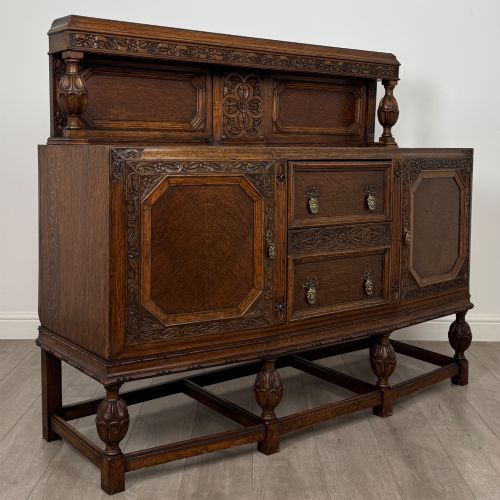 fig 8. A dark carved oak sideboard featuring a raised gallery back, geometric octagonal panel doors, two central drawers with brass handles, and bulbous turned legs.