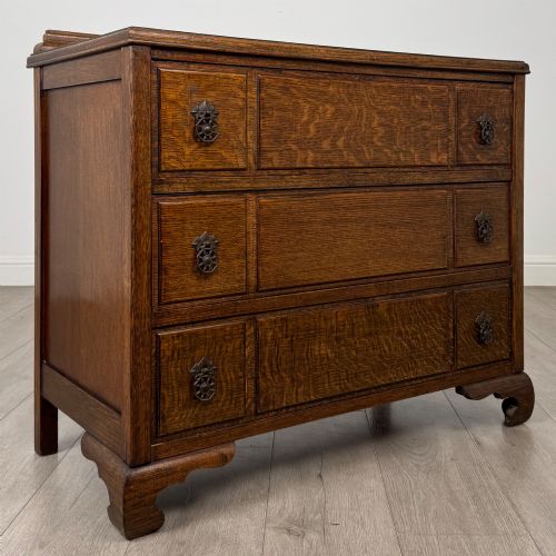 fig 7. A twentieth-century dark oak chest of drawers featuring three drawers with geometric panel moulding, decorative drop handles, and shaped bracket feet.