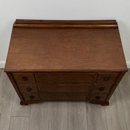 fig 8. A twentieth-century dark oak chest of drawers featuring three drawers with geometric panel moulding, decorative drop handles, and shaped bracket feet.