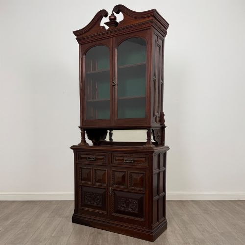 fig 2. A nineteenth-century dark mahogany glazed bookcase featuring a carved swan neck pediment, twin arched glass upper doors, and a lower two-door cabinet with carved panels.