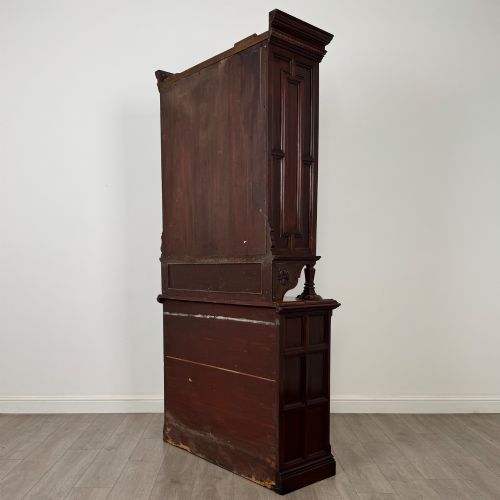 fig 6. A nineteenth-century dark mahogany glazed bookcase featuring a carved swan neck pediment, twin arched glass upper doors, and a lower two-door cabinet with carved panels.