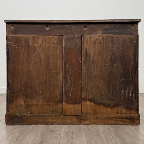 fig 5. A 19th-century Regency mahogany cupboard featuring two frieze drawers, full-length turned flanking columns, and two lower doors set with pleated gold-tone fabric panels on a solid plinth base.