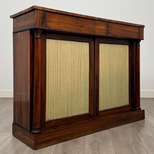 fig 8. A 19th-century Regency mahogany cupboard featuring two frieze drawers, full-length turned flanking columns, and two lower doors set with pleated gold-tone fabric panels on a solid plinth base.