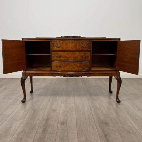 fig 1. A 20th-century burr walnut sideboard featuring three central bowfront drawers flanked by cupboard doors, supported on carved cabriole legs.