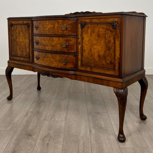 fig 2. A 20th-century burr walnut sideboard featuring three central bowfront drawers flanked by cupboard doors, supported on carved cabriole legs.