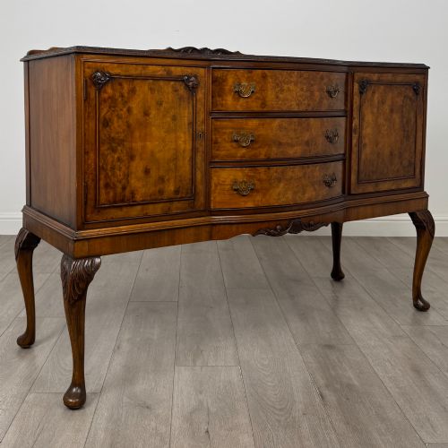 fig 8. A 20th-century burr walnut sideboard featuring three central bowfront drawers flanked by cupboard doors, supported on carved cabriole legs.