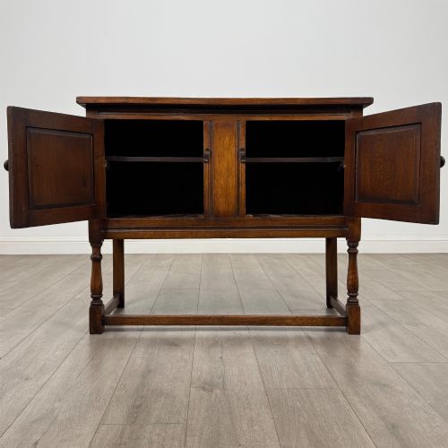 fig 1. A dark oak cupboard featuring two door panels with carved Gothic arch motifs, wooden turn latches, and turned front legs connected by a perimeter stretcher.
