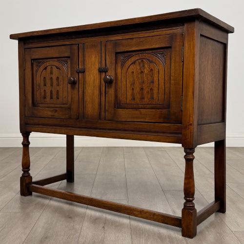 fig 2. A dark oak cupboard featuring two door panels with carved Gothic arch motifs, wooden turn latches, and turned front legs connected by a perimeter stretcher.