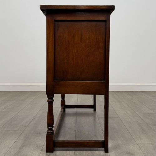 fig 3. A dark oak cupboard featuring two door panels with carved Gothic arch motifs, wooden turn latches, and turned front legs connected by a perimeter stretcher.