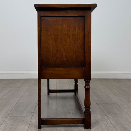 fig 7. A dark oak cupboard featuring two door panels with carved Gothic arch motifs, wooden turn latches, and turned front legs connected by a perimeter stretcher.