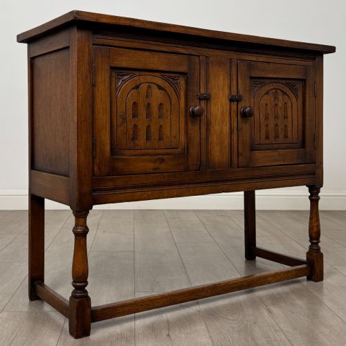 fig 8. A dark oak cupboard featuring two door panels with carved Gothic arch motifs, wooden turn latches, and turned front legs connected by a perimeter stretcher.