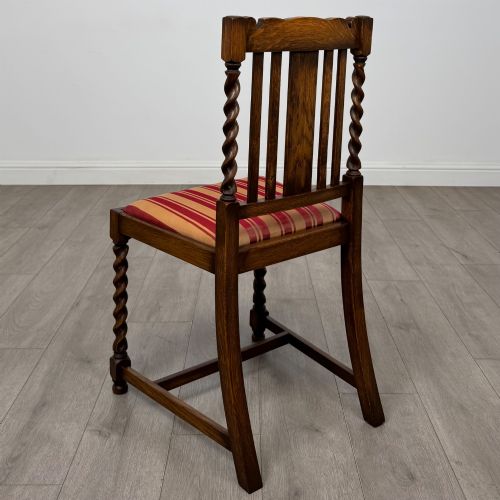 fig 2. A set of four dark oak dining chairs featuring slatted backrests, barley twist front legs, and red and gold striped upholstered seat pads.