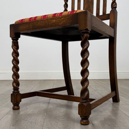 fig 4. A set of four dark oak dining chairs featuring slatted backrests, barley twist front legs, and red and gold striped upholstered seat pads.