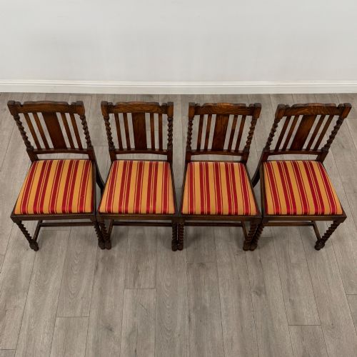 fig 6. A set of four dark oak dining chairs featuring slatted backrests, barley twist front legs, and red and gold striped upholstered seat pads.