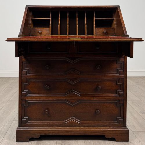fig 1. A dark oak Jacobean style slant-front bureau featuring geometric inlaid panels and four drawer fronts with turned wooden knobs.